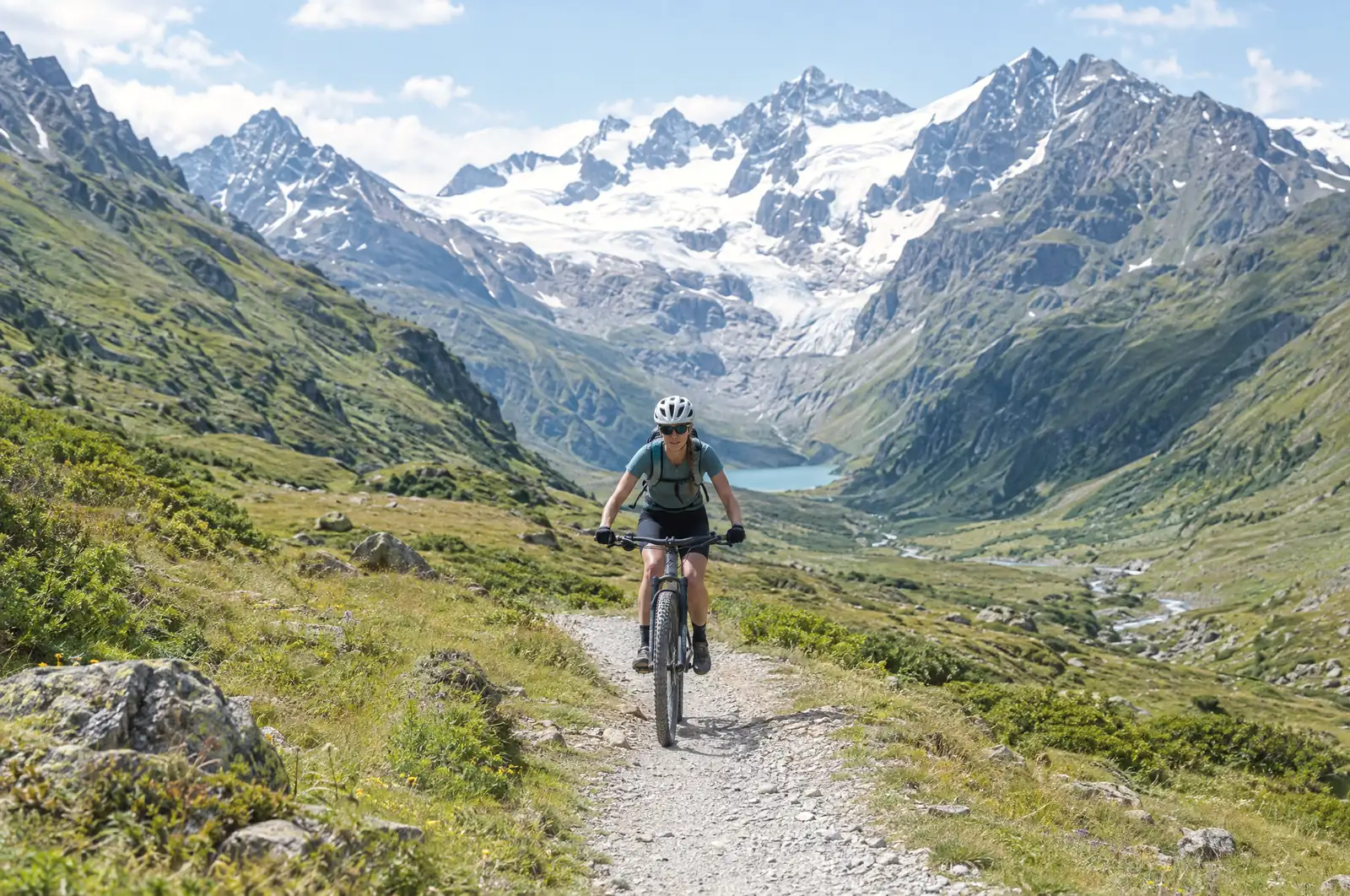 Cyklistka na štěrkové cestě vysokohorským údolím, v pozadí ledovec